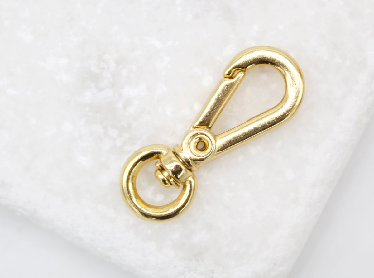 A shiny gold lobster swivel clasp rests against a textured white background.