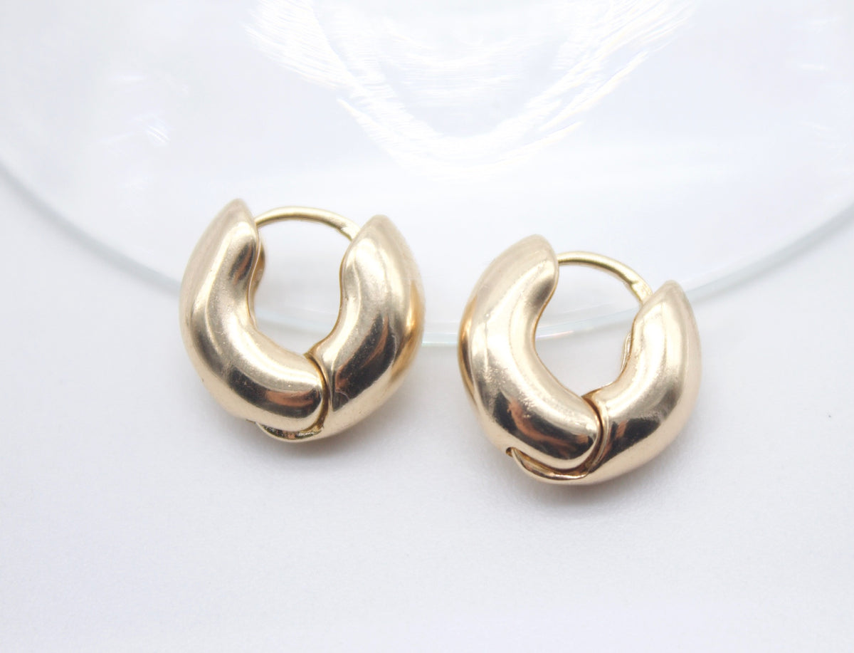 A pair of chunky gold hoop earrings rests against a clean white background.