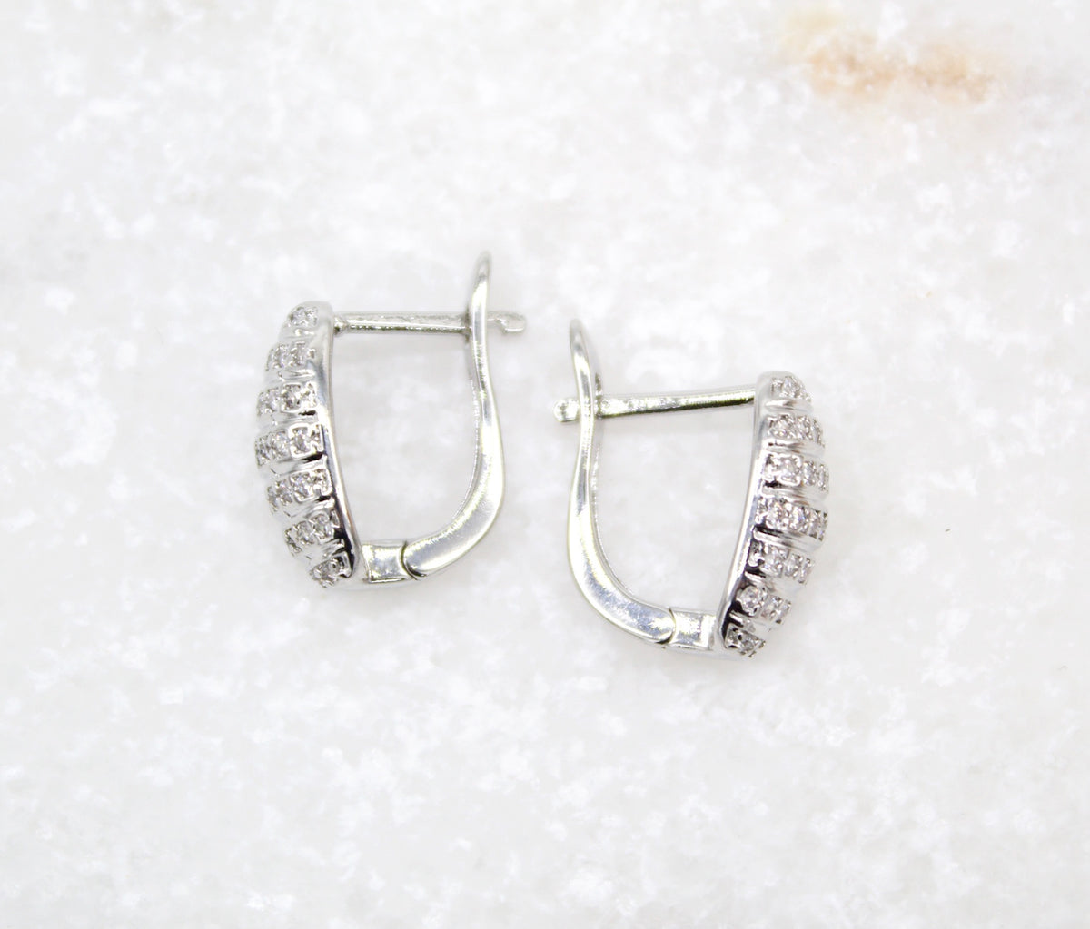 A pair of shimmering white gold hoop earrings embellished with small sparkling diamonds lies flat on a light marble surface.
