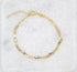 A delicate gold chain bracelet features alternating multi-toned heart charms and rests on a textured white marble surface.