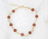 A gold chain bracelet features sparkling brown sandstone gemstone beads arranged in a circle on a white background.