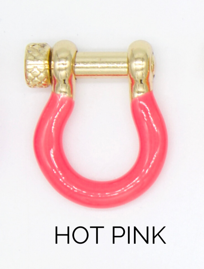 A hot pink enamel and gold-plated U-shaped shackle charm rests against a white background.