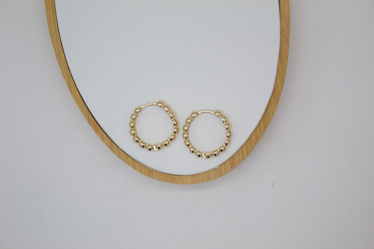 Two textured gold hoop earrings rest side by side on a white oval tray with a wooden frame.