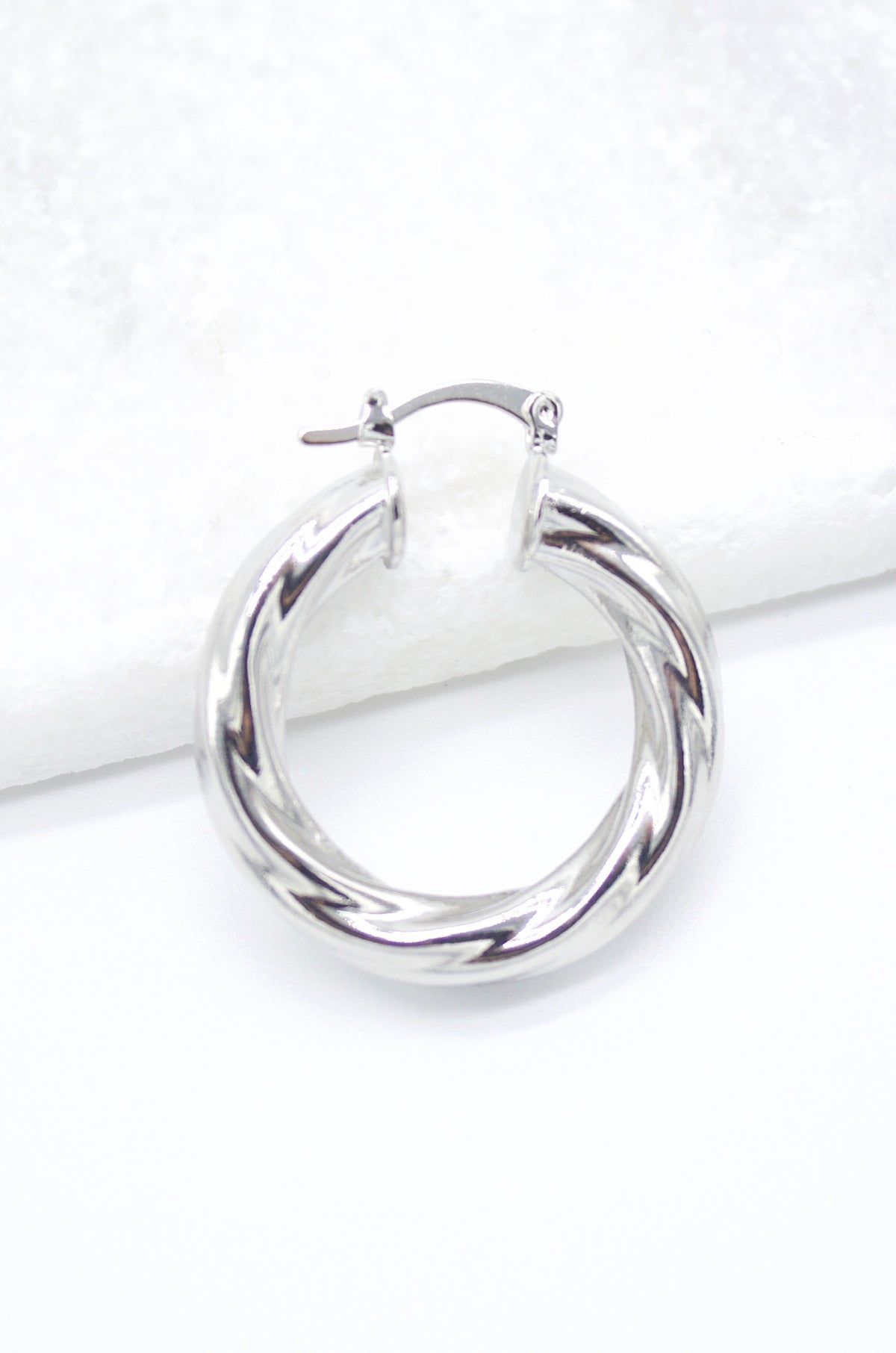 A polished silver twisted hoop earring rests on a clean white surface.