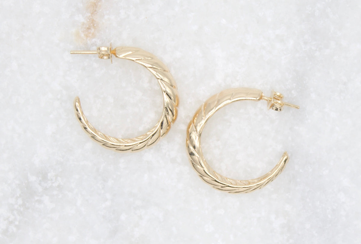 A pair of textured gold hoop earrings rests on a light marble surface.