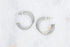 A pair of silver triple hoop earrings rests on a textured white marble surface.