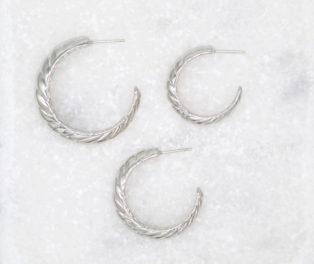 Three silver twist hoop earrings display their textured patterns against a light textured surface.