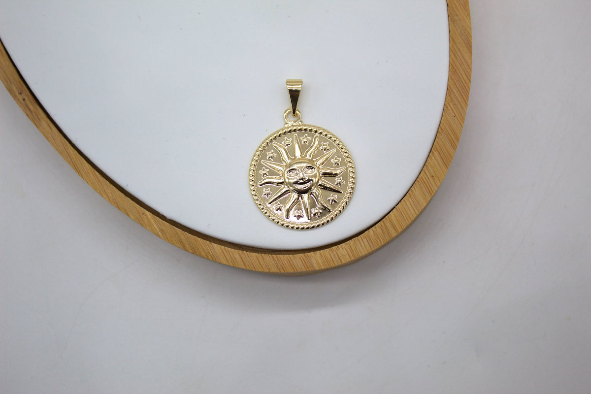 A round gold sun pendant rests on a white display surface with a wooden frame.