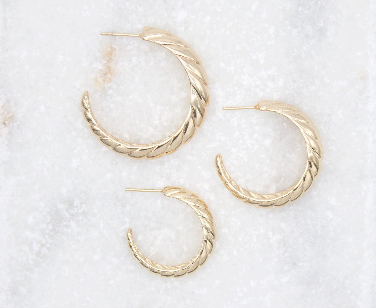 Three polished gold twisted hoop earrings rest on a white marble surface.