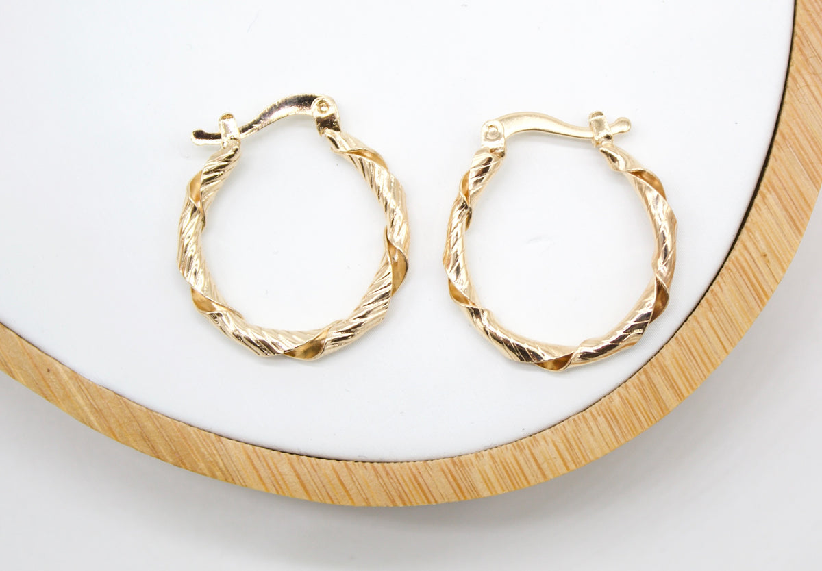 A pair of twisted gold hoop earrings rests neatly on a white display tray with a wooden rim.