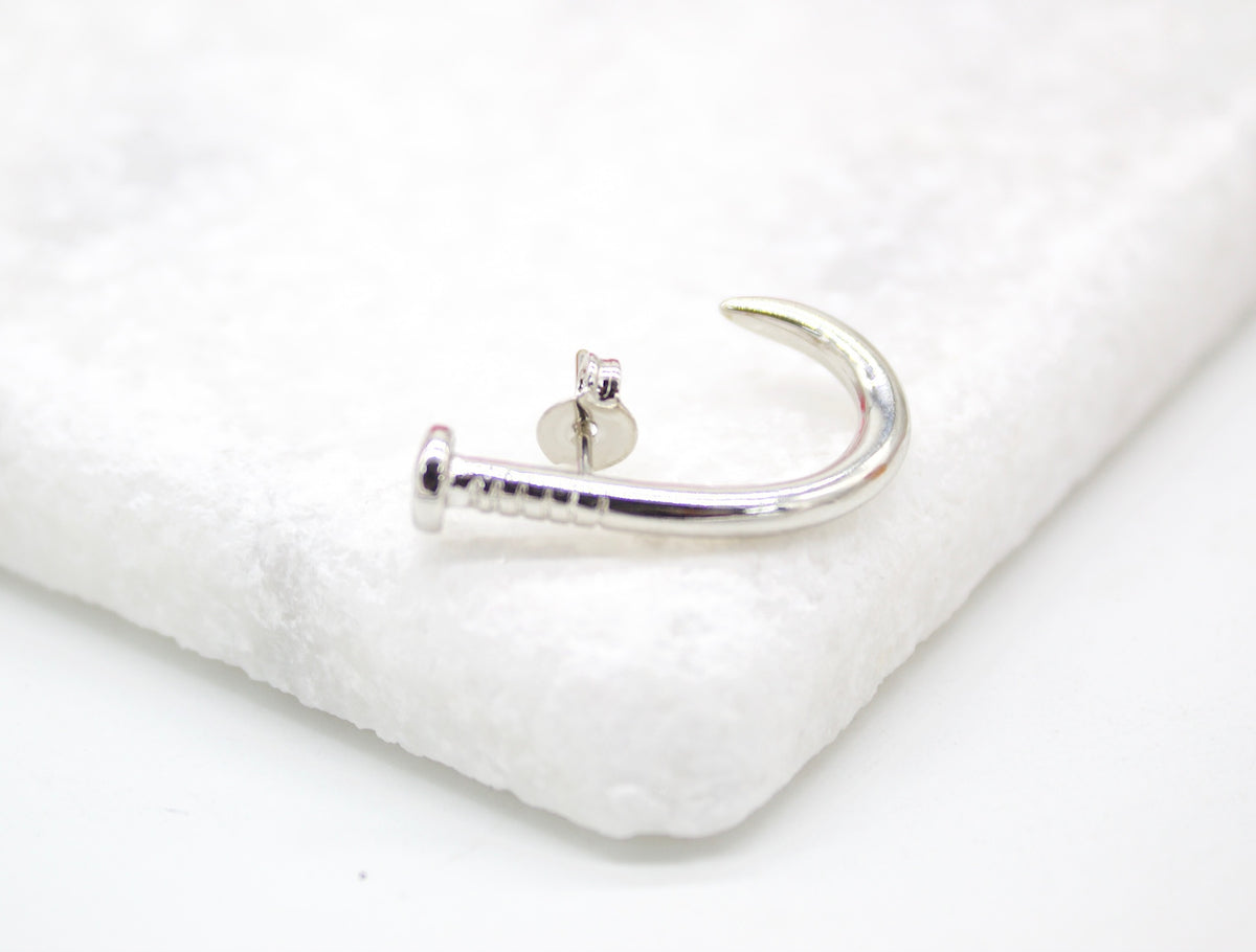 A polished silver nail-shaped earring rests on a textured white surface.