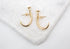 A pair of gold nail-shaped stud earrings rests on a textured white marble surface.