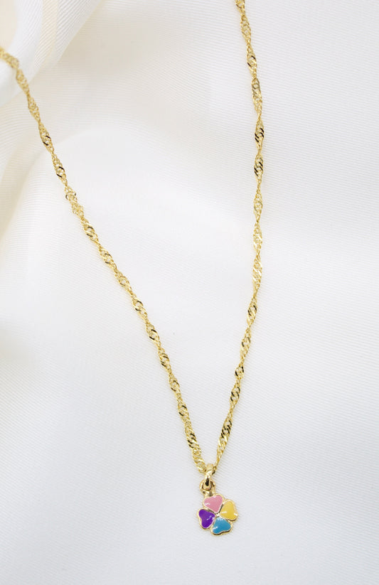 A delicate gold chain necklace drapes against a soft white background, showcasing a colorful four-leaf clover pendant with pink, yellow, purple, and blue enamel petals.