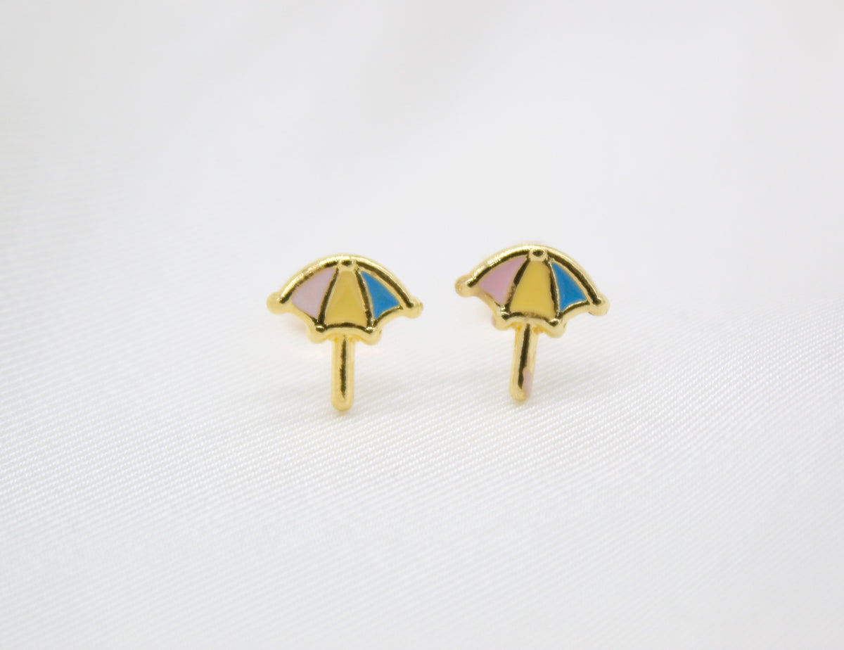 A pair of gold stud earrings shaped like colorful little umbrellas rests on a white background.