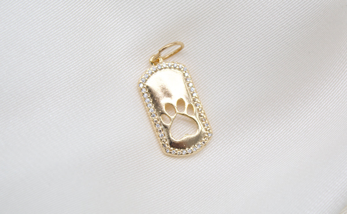 A gold paw print pendant necklace sparkles against a soft, textured white fabric background.