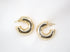 A pair of chunky gold hoop earrings rests on a textured white silk background.