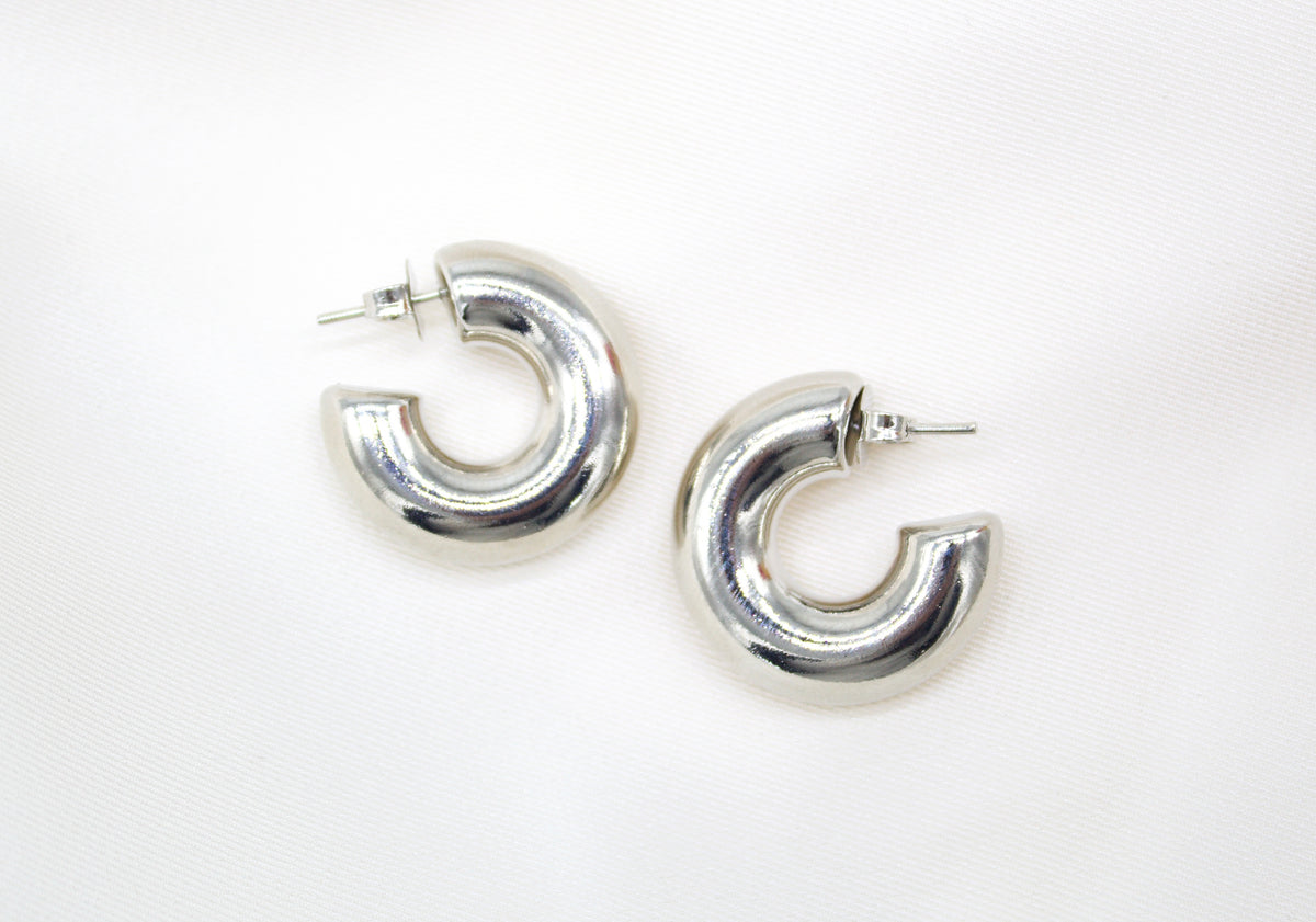 Two polished silver hoop earrings rest on a soft white background.