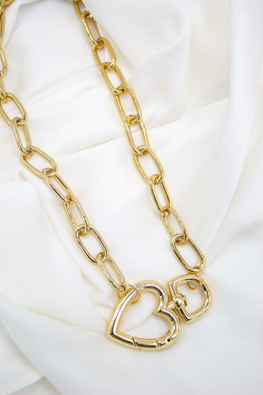 A chunky gold chain necklace featuring two interlocking heart pendants rests gracefully on a white silk background.