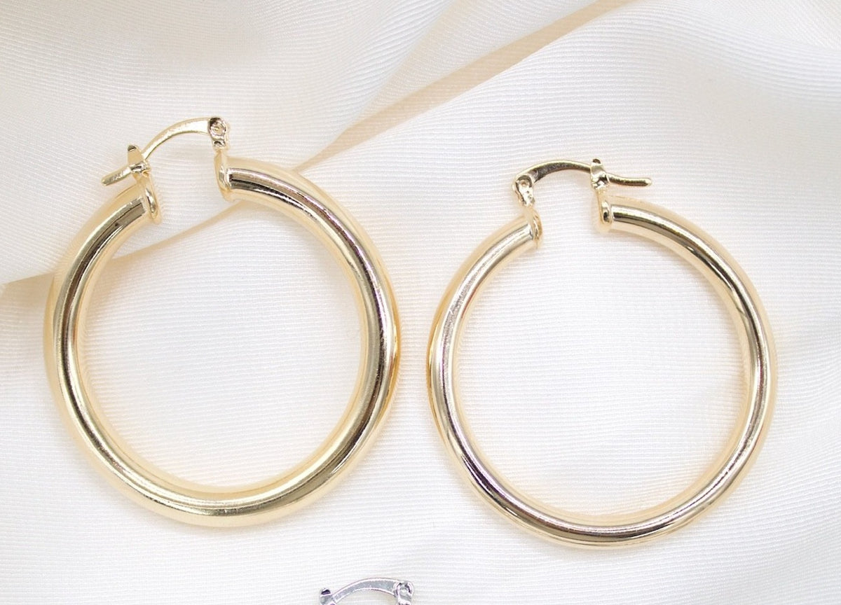 Two polished gold hoop earrings rest on a textured white fabric background.