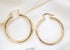 Two polished gold hoop earrings rest on a textured white fabric background.