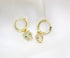 A pair of gold hoop earrings featuring crystal-pave panther charms with vibrant green eyes rests on a soft white satin background.
