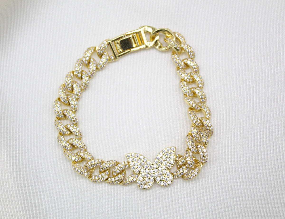 A dazzling gold cuban link bracelet embellished with sparkling cubic zirconia stones rests on a white background, featuring a prominent diamond-paved butterfly charm.