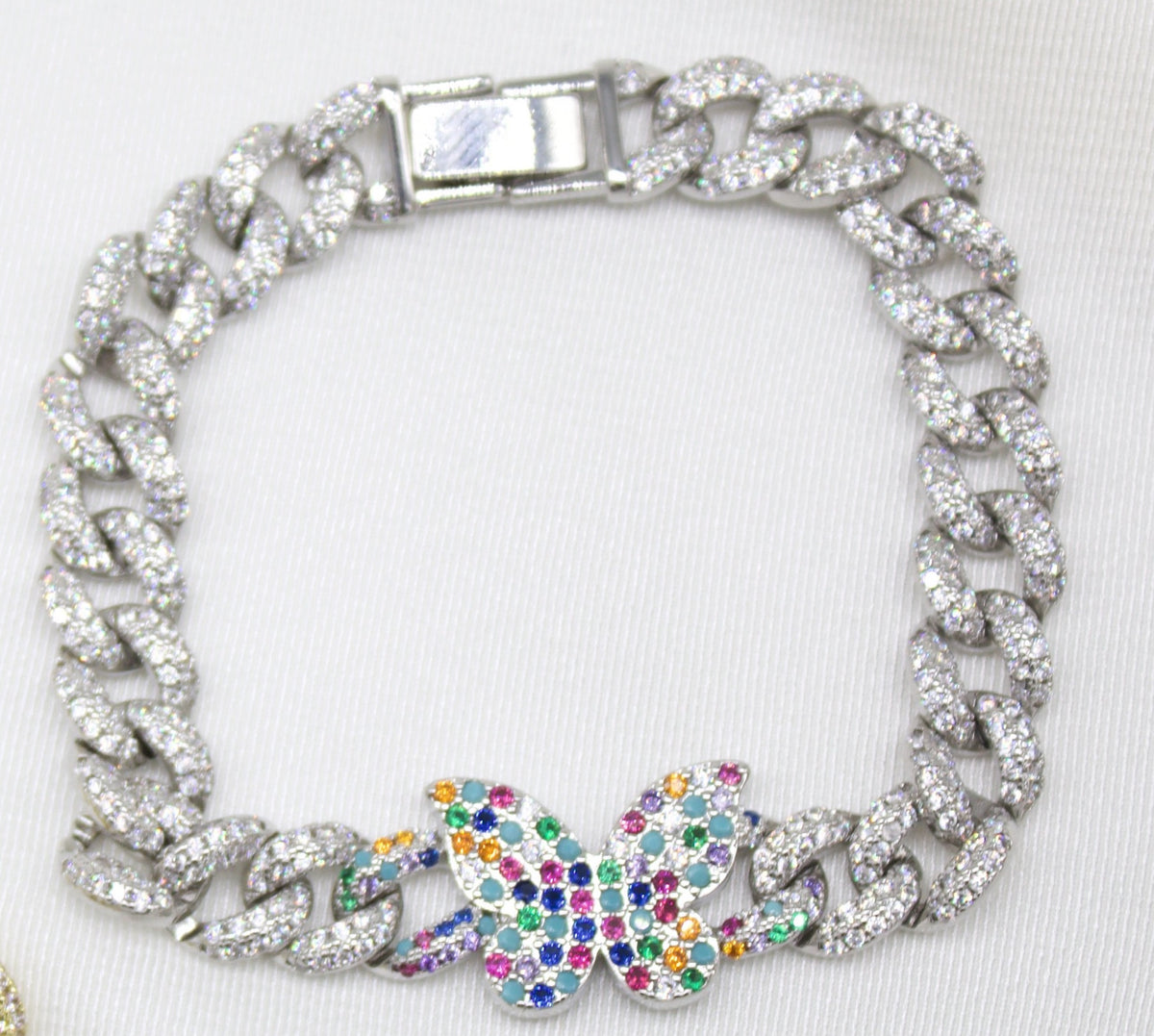 A diamond-pave cuban link bracelet features a multicolored, gemstone-encrusted butterfly charm on a white background.