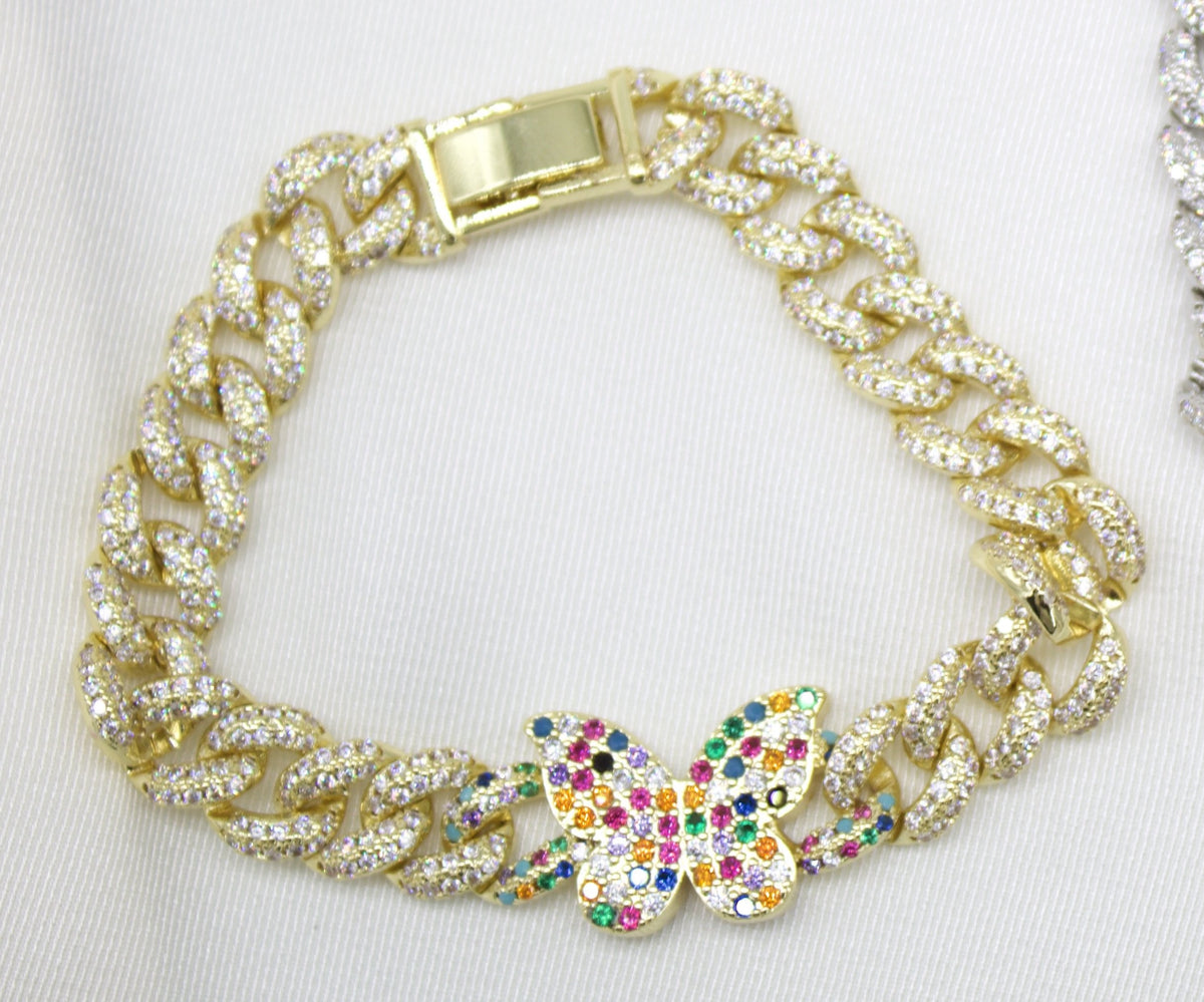 A gold cuban link bracelet encrusted with sparkling cubic zirconia stones features a colorful, jewel-toned butterfly charm centered on a white background.