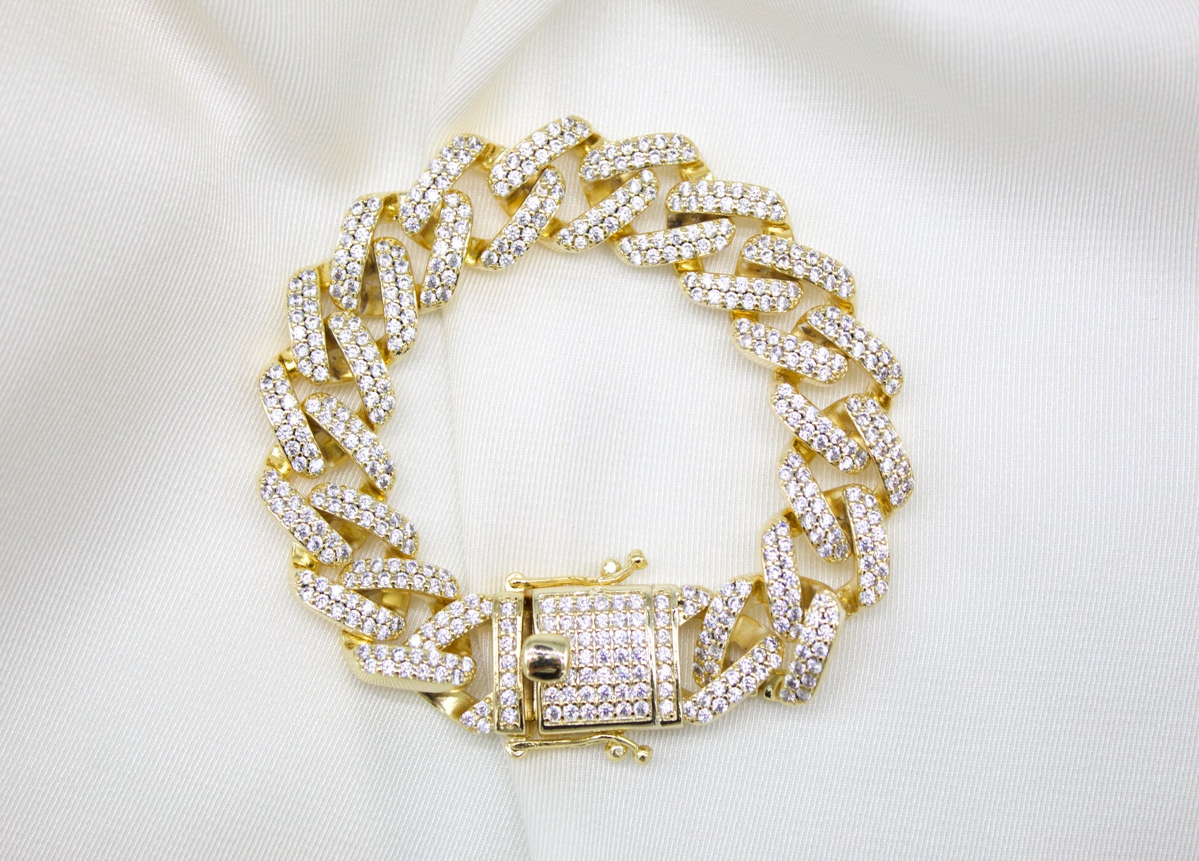A sparkling gold cuban link bracelet encrusted with cubic zirconia stones rests gracefully on white satin.