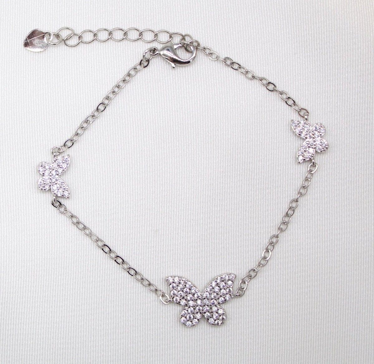 A delicate silver butterfly charm bracelet sparkles with pavé crystals on a white fabric background.