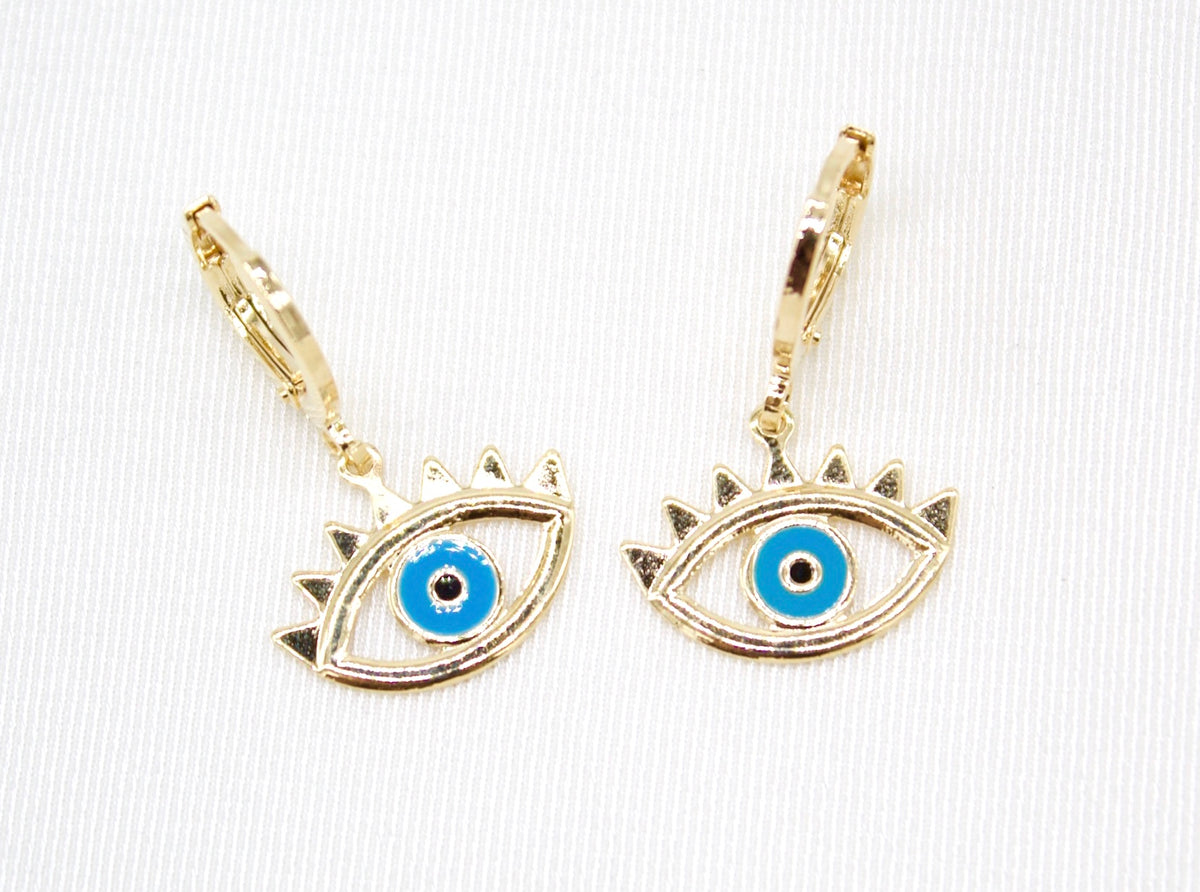 A pair of gold evil eye hoop earrings rest on a white fabric surface.