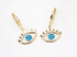 A pair of gold evil eye hoop earrings rest on a white fabric surface.