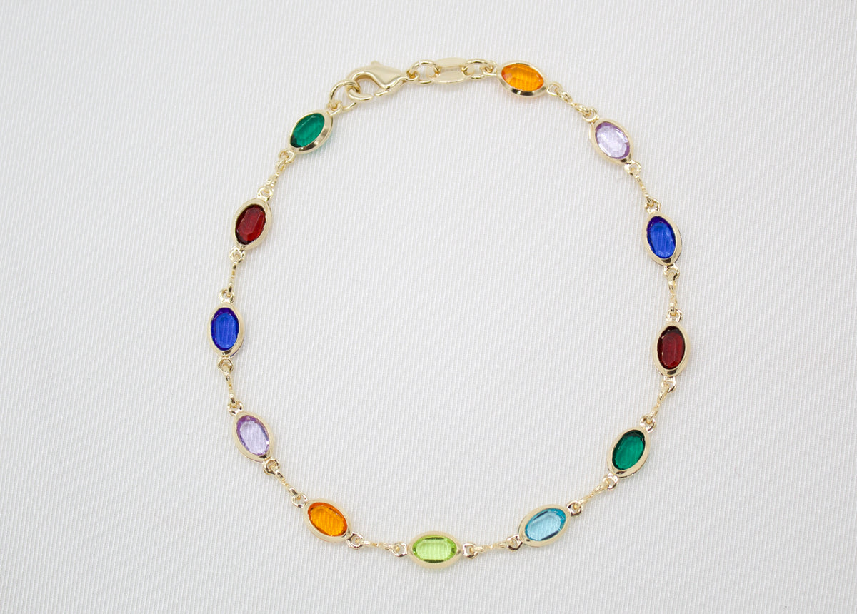 A delicate gold chain bracelet features an array of colorful multi-gemstone stations against a neutral white background.