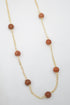 A delicate gold chain necklace features evenly spaced round brown sandstone beads against a white background.