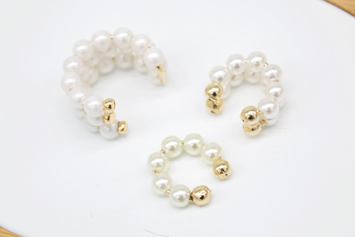 A set of three elegant faux-pearl ear cuffs features delicate gold-toned accents arranged on a clean white surface.