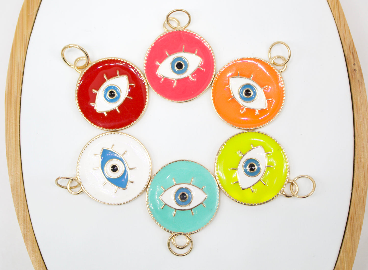 Six colorful enamel evil eye charms with gold loops are arranged in a circle on a white display.