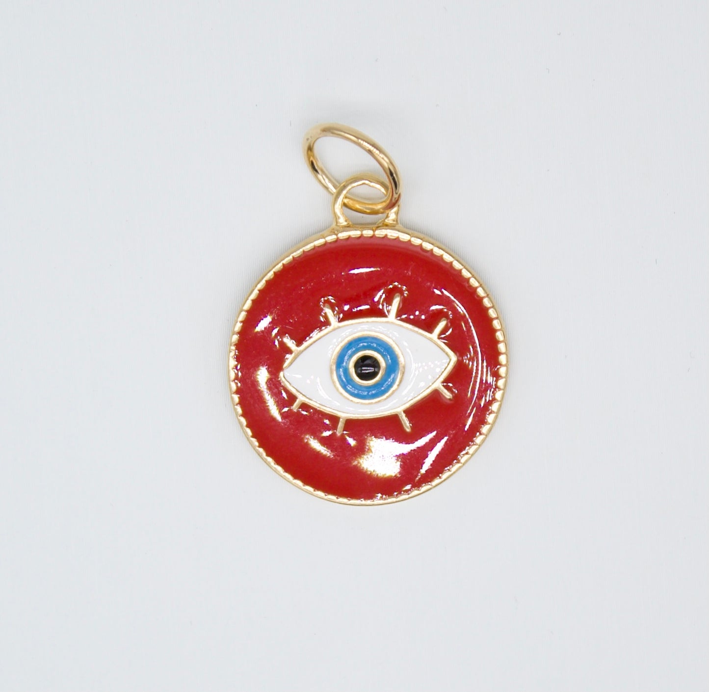A gold-rimmed red enamel evil eye pendant features a central blue and white eye design against a glossy background.