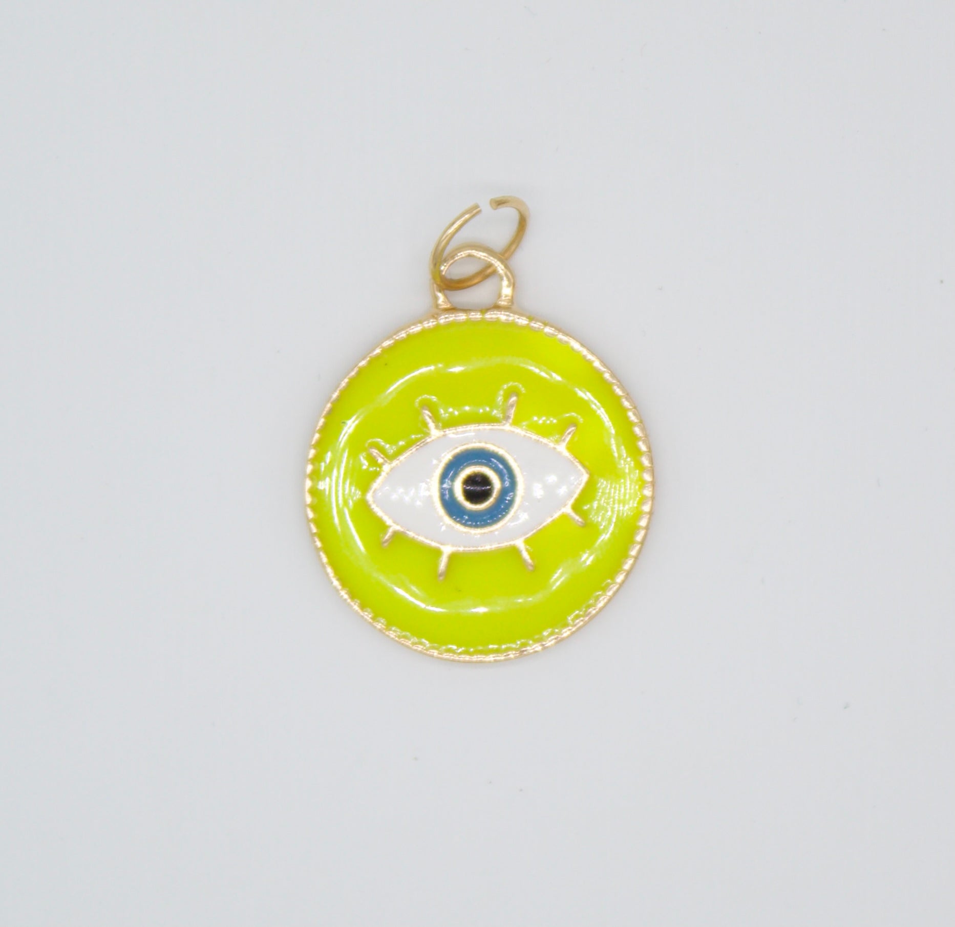 A round chartreuse and gold pendant displays a stylized evil eye charm with blue, white, and black enamel.