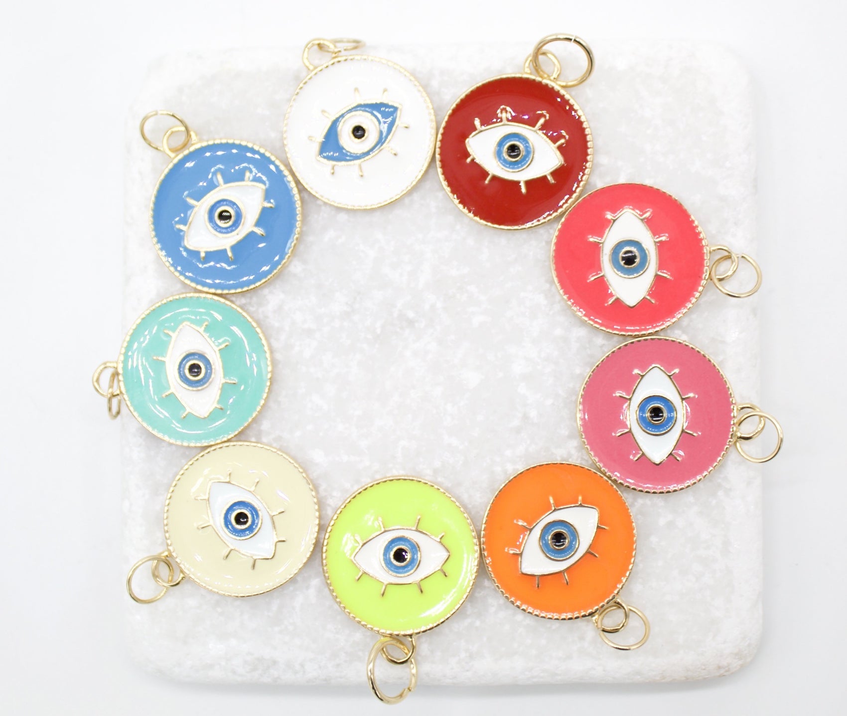 A vibrant collection of colorful enamel evil eye charms arranged in a circle on a white marble surface.