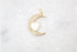 A delicate gold crescent moon pendant sparkles with pavé crystals, featuring a glossy white enamel heart nestled in the center against a textured white marble background.