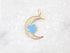 A gold crescent moon pendant rests on a white marble surface, featuring pavé-set CZ stones and a central light blue heart charm.