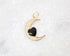 A gold crescent moon pendant encrusted with cubic zirconia crystals features a glossy black heart charm resting in its center against a white marble background.