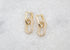 A pair of interlocking gold chain-link huggie earrings encrusted with sparkling pave stones rests on a textured white marble surface.