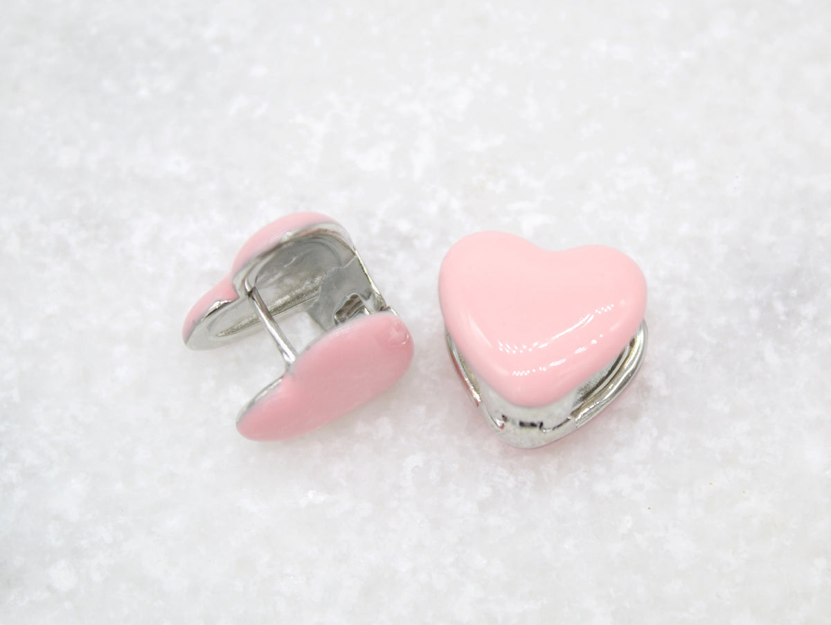 A pair of charming pink enamel heart huggie earrings rests on a textured white surface.