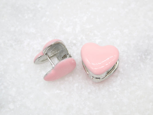 A pair of charming pink enamel heart huggie earrings rests on a textured white surface.