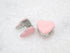 A pair of charming pink enamel heart huggie earrings rests on a textured white surface.