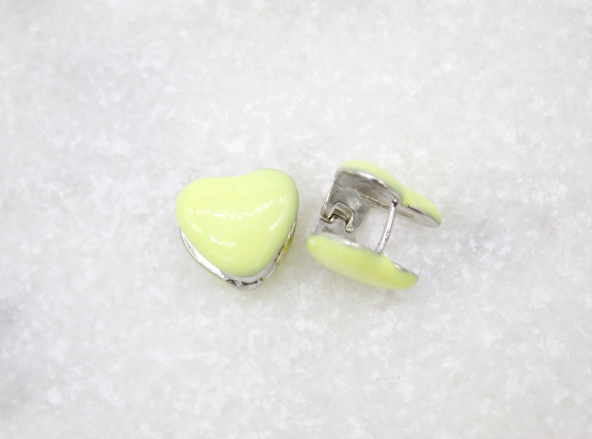 A pair of cute pastel yellow heart-shaped huggie hoop earrings rest on a white marble surface.