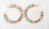 A pair of gold hoop earrings embellished with colorful enamel leaves rests on a textured white surface.