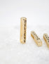 A vertical gold rectangular pendant with the word "BELIEVE" stamped on it rests on a white surface alongside two other similar pendants.