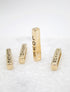 Four gold bar pendants engraved with the words "LOVE," "FAITH," "BELIEVE," and "ACTION" stand upright on a textured white surface.